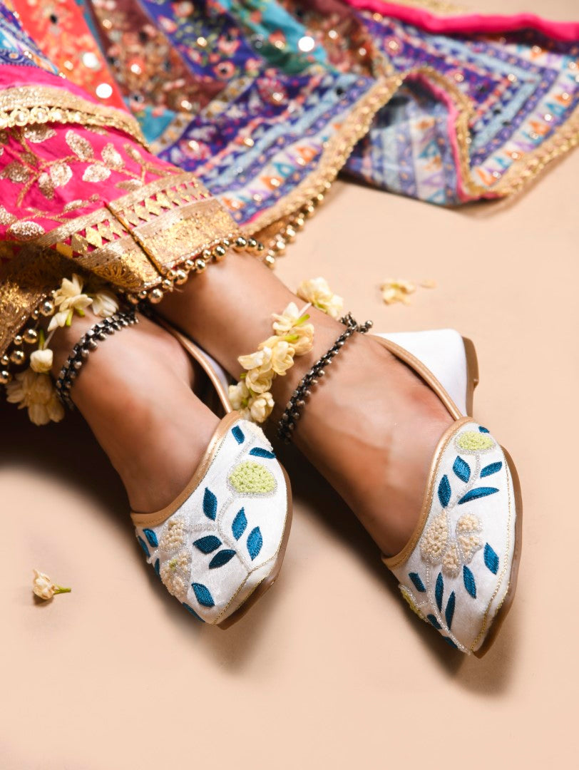 exquisitely embroidered juttis featuring floral and leaf patterns
White