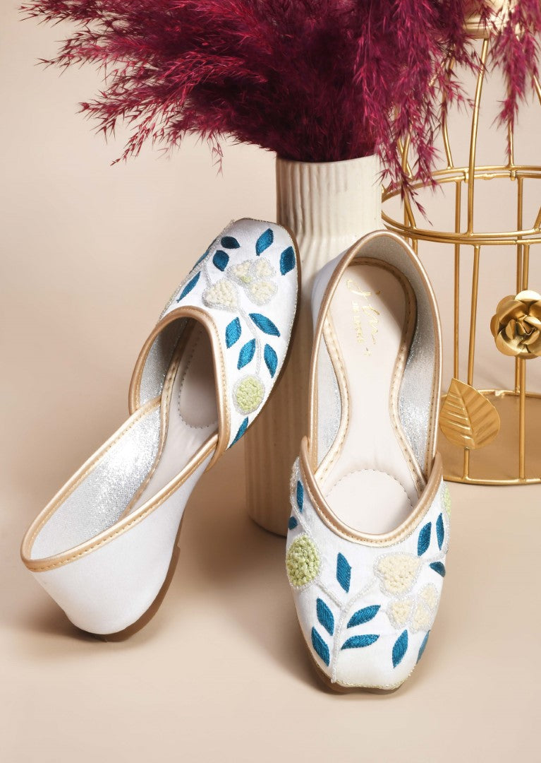 exquisitely embroidered juttis featuring floral and leaf patterns
White