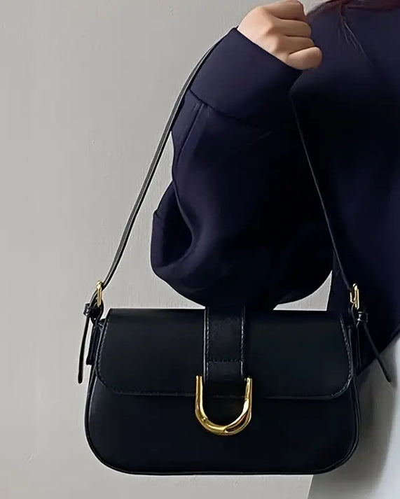 Black crossbody shoulder bag with gold U-shaped buckle, adjustable strap, and glossy leather finish for women