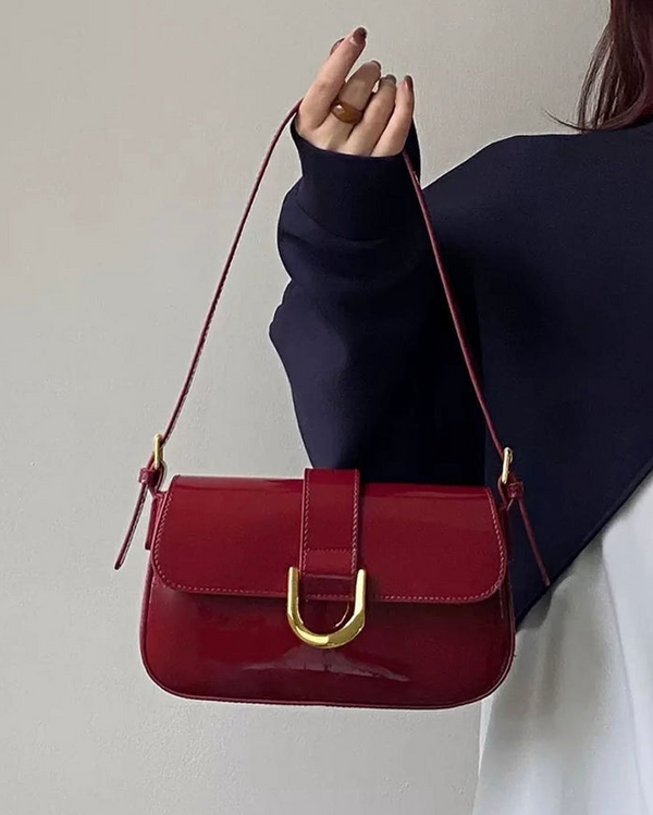 Red crossbody shoulder bag with gold U-shaped buckle, adjustable strap, and glossy leather finish for women