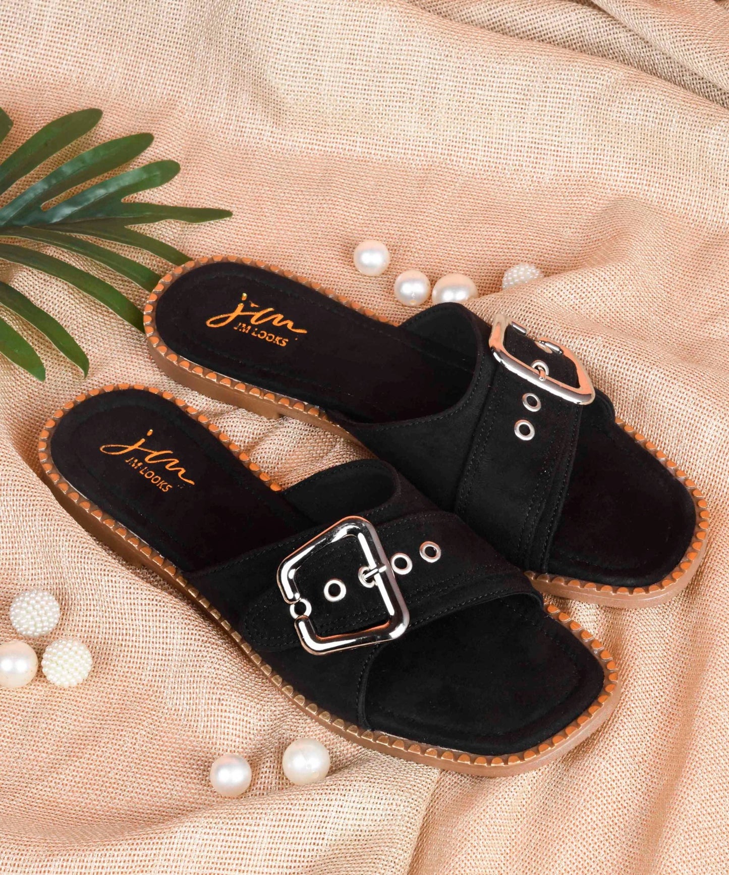 Black slip-on flat sandal featuring oversized silver buckle, metal eyelet detailing, suede strap, and contrast stitched sole.