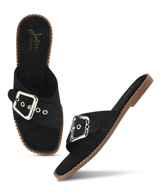 Black slip-on flat sandal featuring oversized silver buckle, metal eyelet detailing, suede strap, and contrast stitched sole.