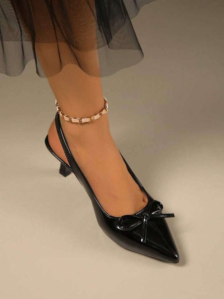 Black patent slingback heels with pointed toe, decorative bow detail, glossy finish, elegant stiletto silhouette.