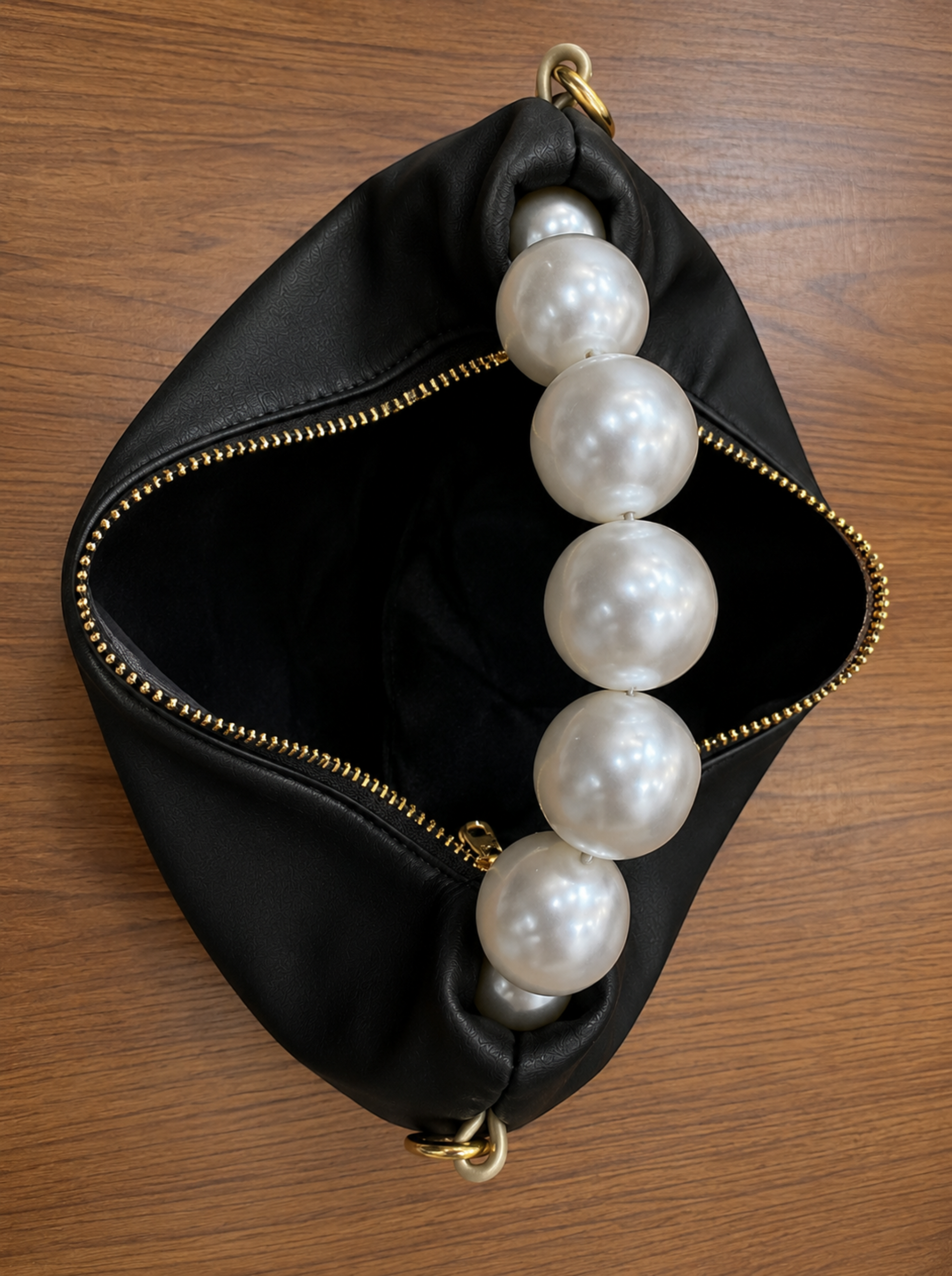 Pearl handle bag in black faux leather held by hand showing soft hobo silhouette gold zipper