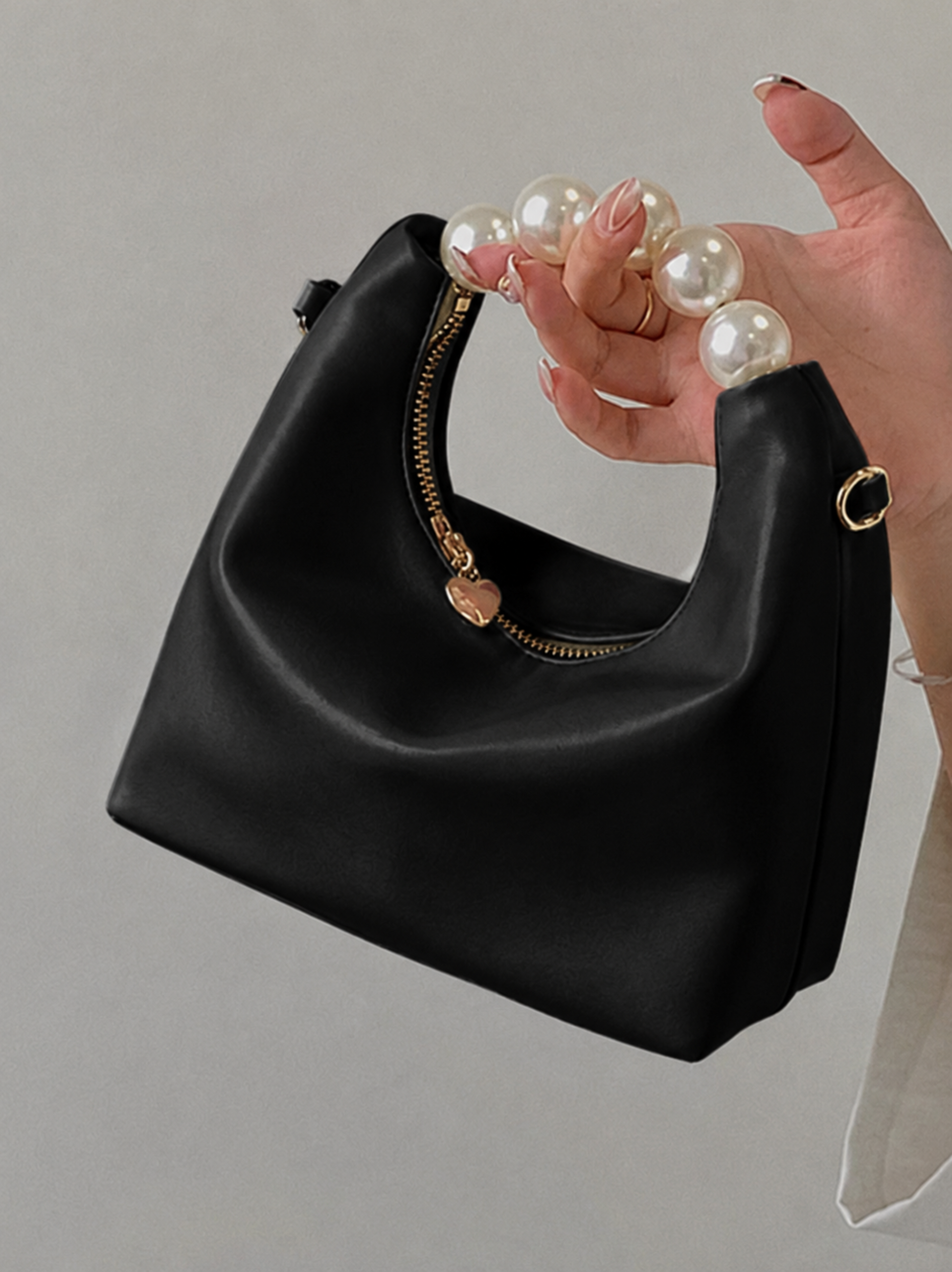 Pearl handle bag in black faux leather held by hand showing soft hobo silhouette gold zipper