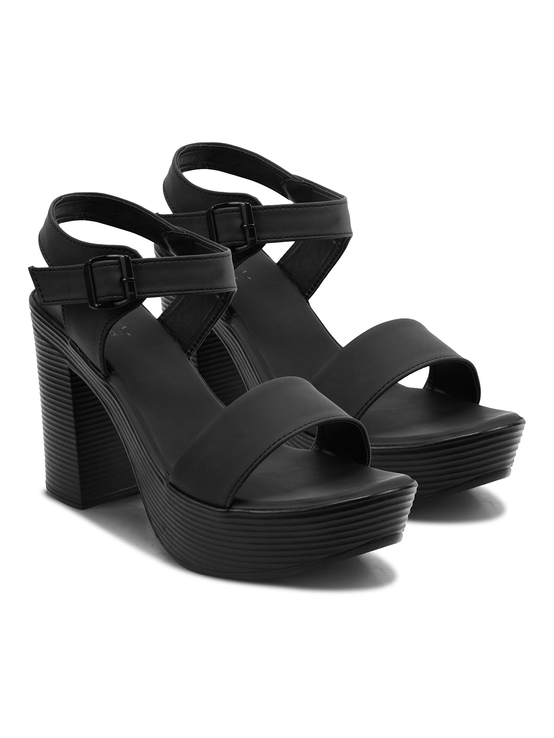 Woman wearing black chunky platform block heels with open toe and ankle buckle strap, styled with skirt