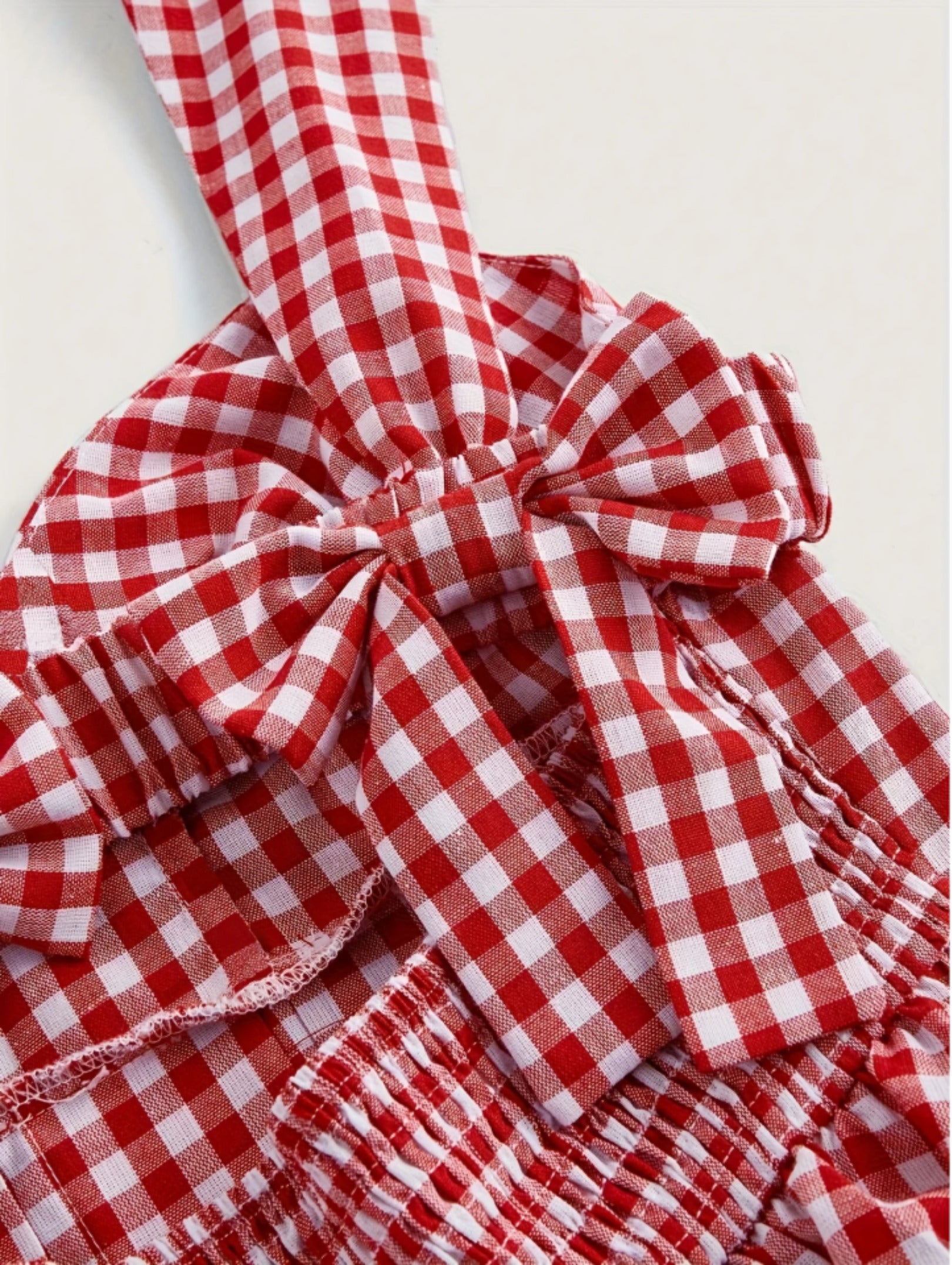 Red gingham sleeveless mini dress with bow detail, sweetheart neckline, wide straps, and flared A-line skirt