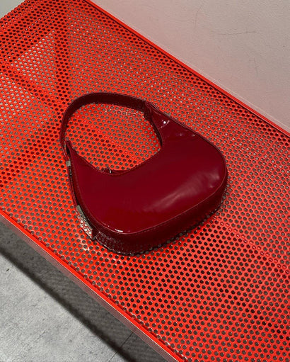 Burgundy half moon handbag for women in glossy patent finish with curved crescent shape and dual zip pulls.