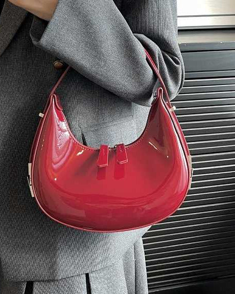 Red half moon handbag for women in glossy patent finish with curved crescent shape and dual zip pulls.