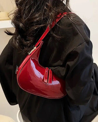 Burgundy half moon handbag for women in glossy patent finish with curved crescent shape and dual zip pulls.