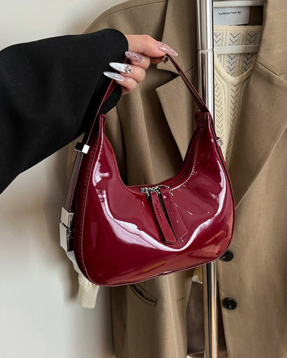Wine-Red half moon handbag for women in glossy patent finish with curved crescent shape and dual zip pulls.