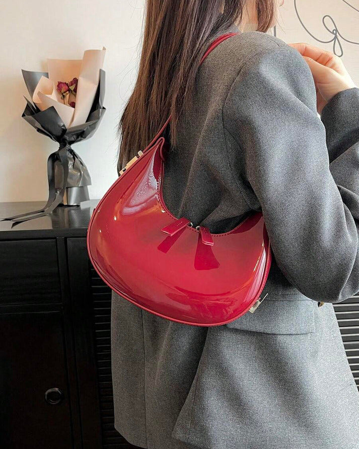 Red half moon handbag for women in glossy patent finish with curved crescent shape and dual zip pulls.