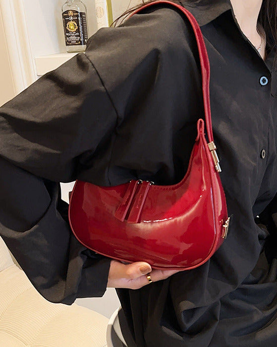 Burgundy half moon handbag for women in glossy patent finish with curved crescent shape and dual zip pulls.
