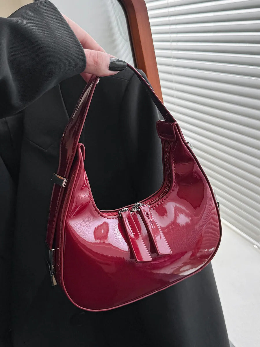 Wine-Red half moon handbag for women in glossy patent finish with curved crescent shape and dual zip pulls.