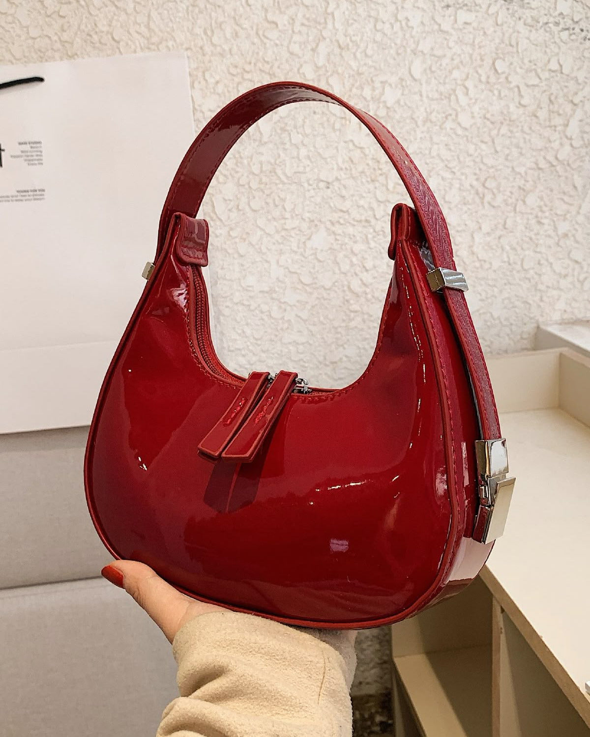 Burgundy half moon handbag for women in glossy patent finish with curved crescent shape and dual zip pulls.