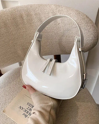 White half moon handbag for women in glossy patent finish with curved crescent shape and dual zip pulls.