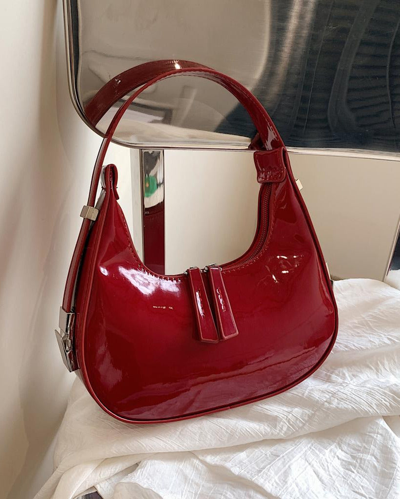 Burgundy half moon handbag for women in glossy patent finish with curved crescent shape and dual zip pulls.