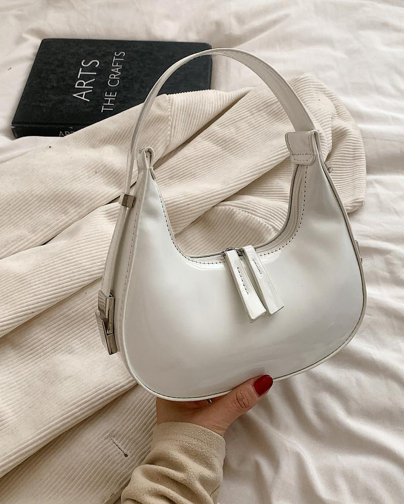 White half moon handbag for women in glossy patent finish with curved crescent shape and dual zip pulls.