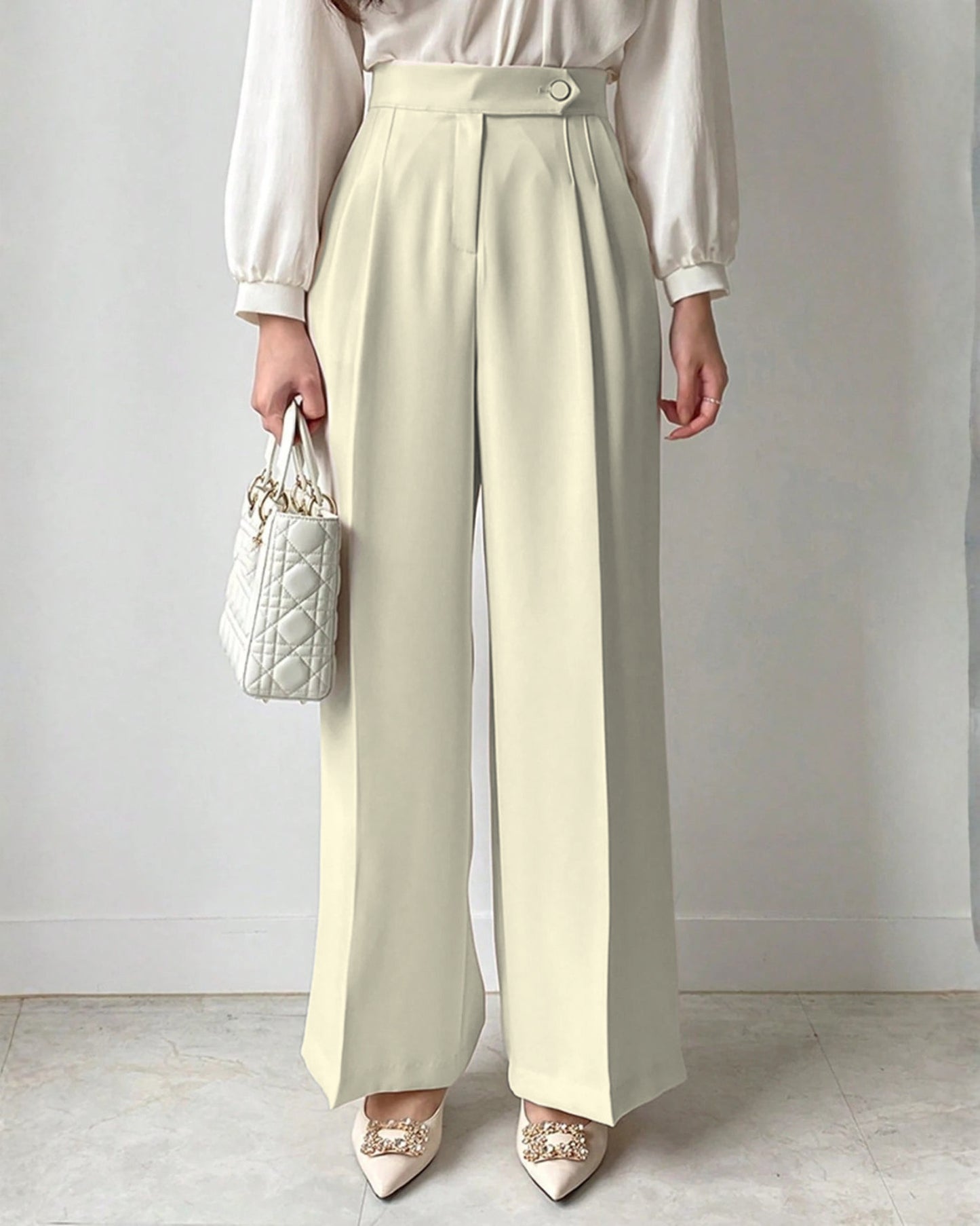 Cream high-waisted wide-leg pleated trousers for women styled with white blouse and embellished pointed satin heels