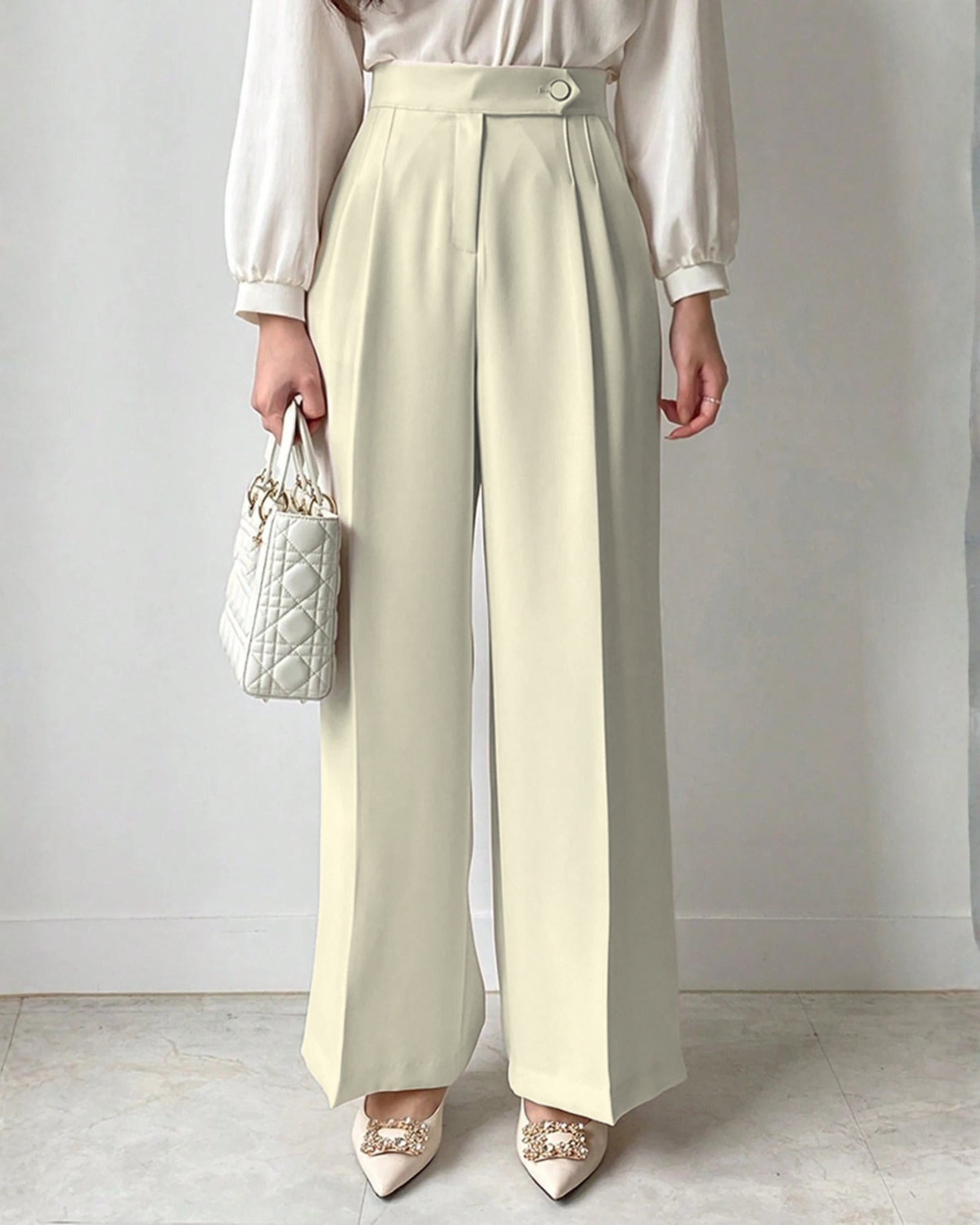 Cream high-waisted wide-leg pleated trousers for women styled with white blouse and embellished pointed satin heels