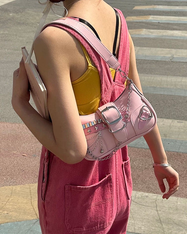 Baguette bag in pink featuring silver studs, star accents, buckle detail, layered chains, and heart charm