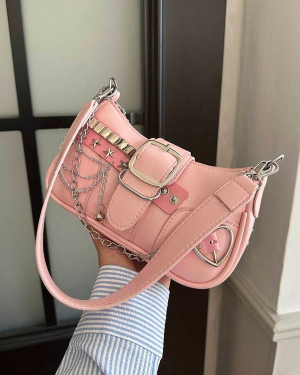 Baguette bag in pink featuring silver studs, star accents, buckle detail, layered chains, and heart charm