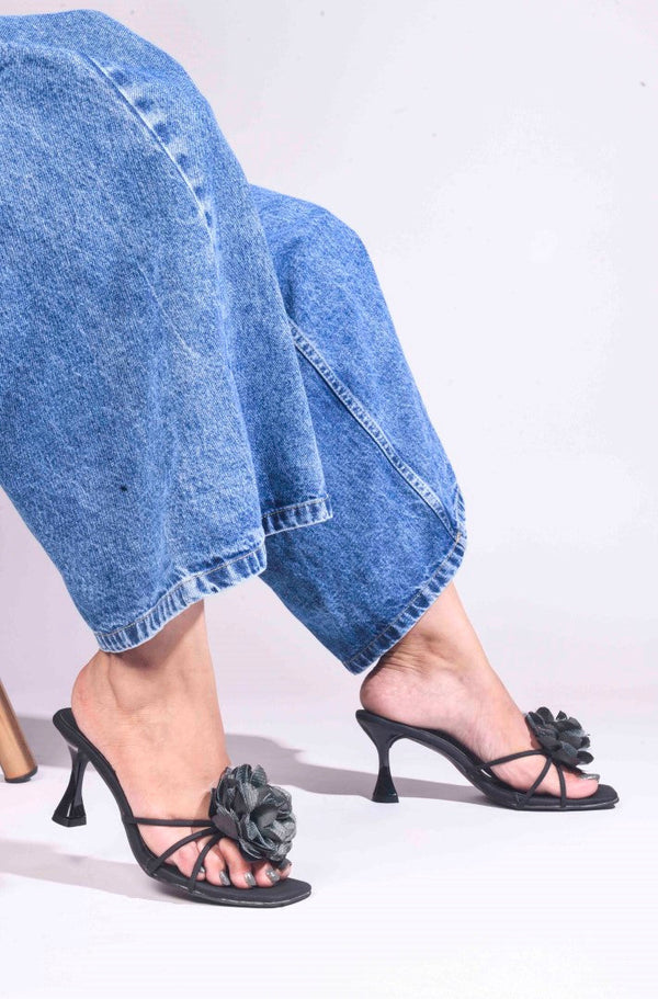 women's heeled mules featuring a large floral embellishment on the strap
 Black
