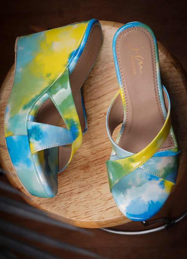 Platform wedge heels in blue yellow watercolor print with criss cross straps, open toe slip-on design.
