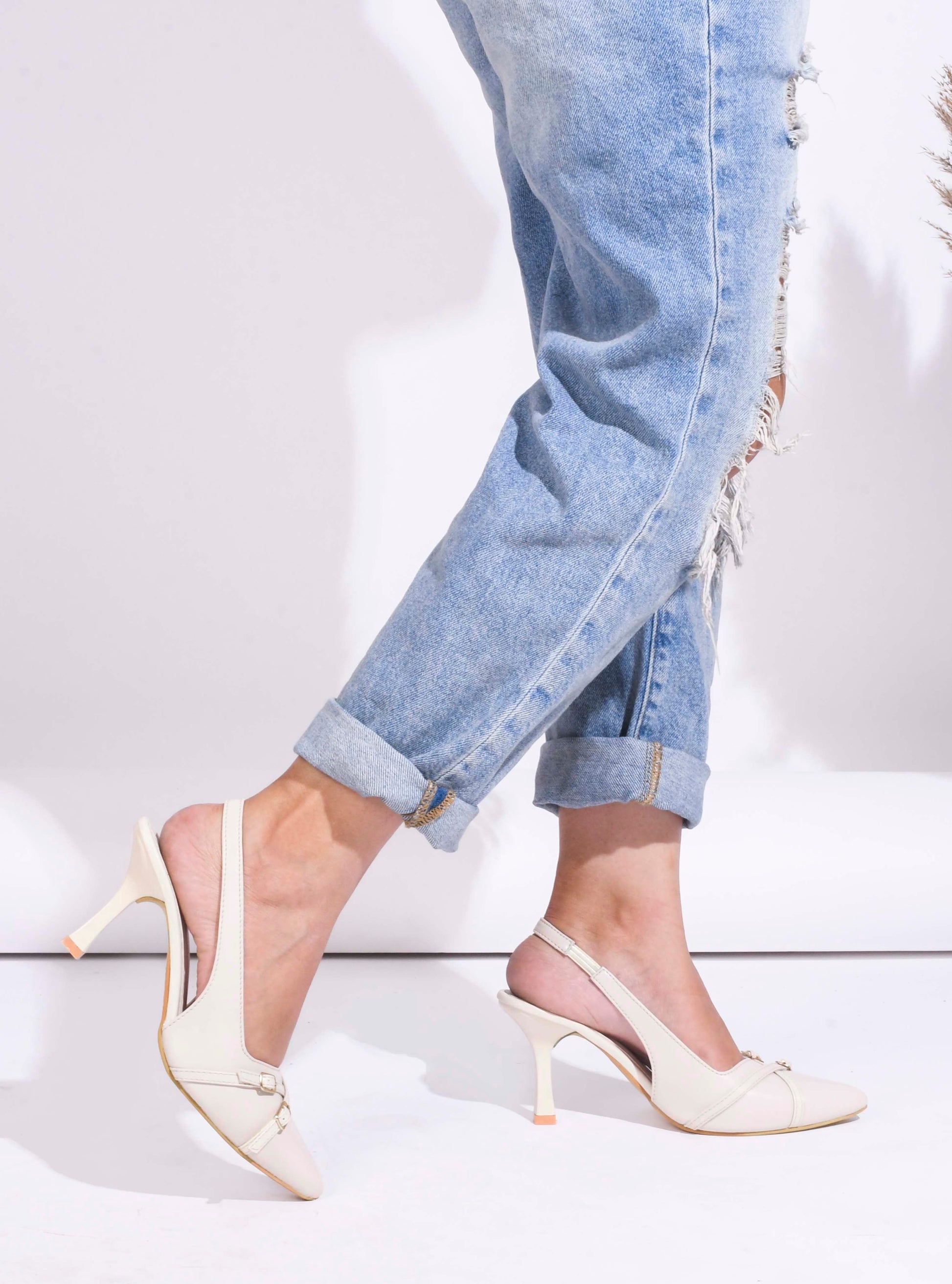 A pointed-toe slingback heel with strap and buckle details on the vamp and an adjustable strap
 Cream