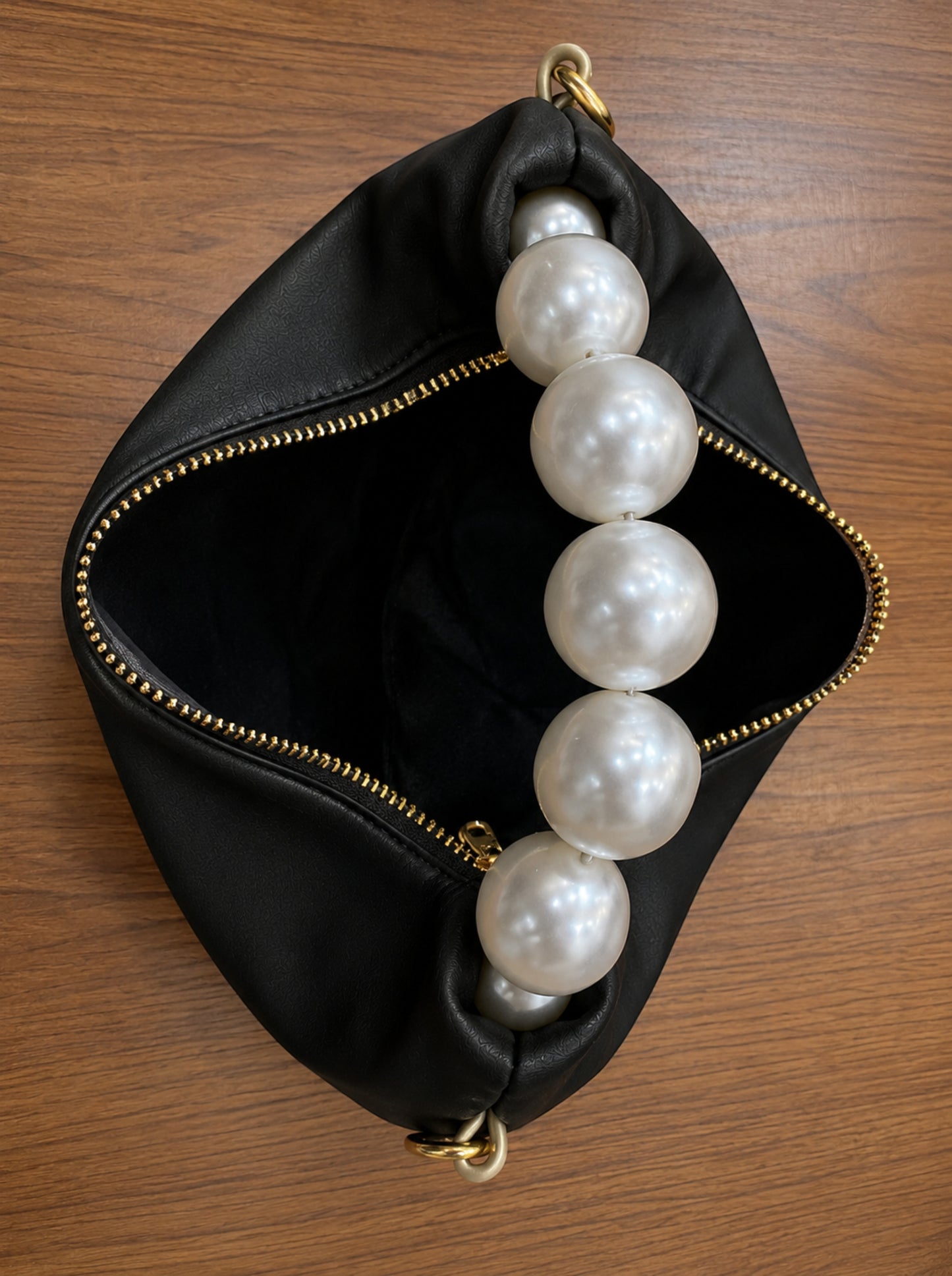 Pearl handle bag in black faux leather held by hand showing soft hobo silhouette gold zipper