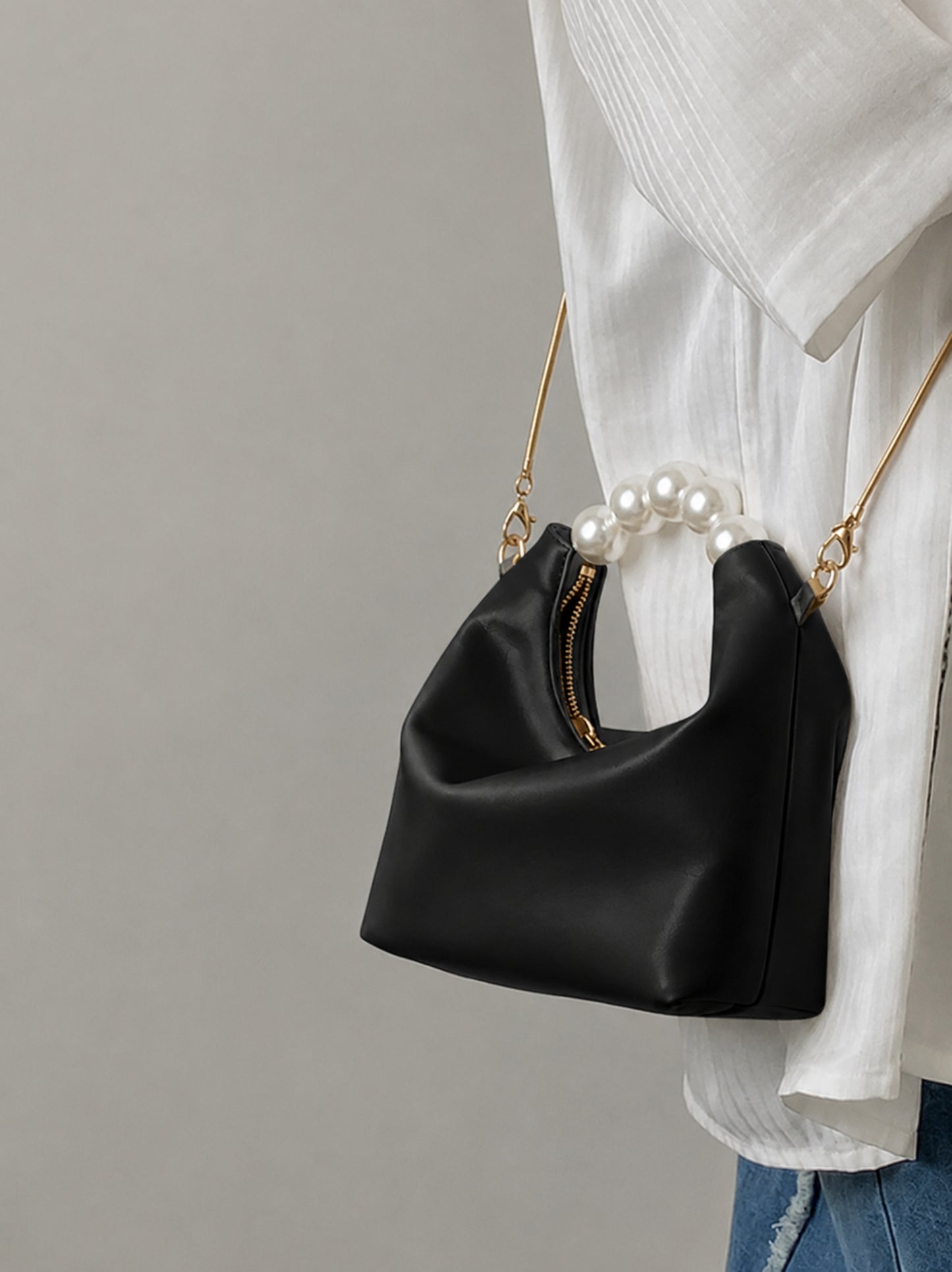 Pearl handle bag in black faux leather held by hand showing soft hobo silhouette gold zipper