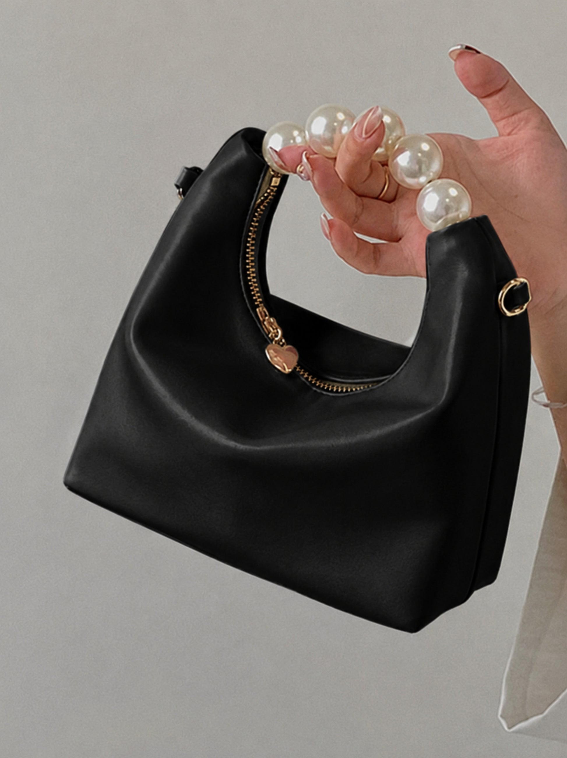 Pearl handle bag in black faux leather held by hand showing soft hobo silhouette gold zipper