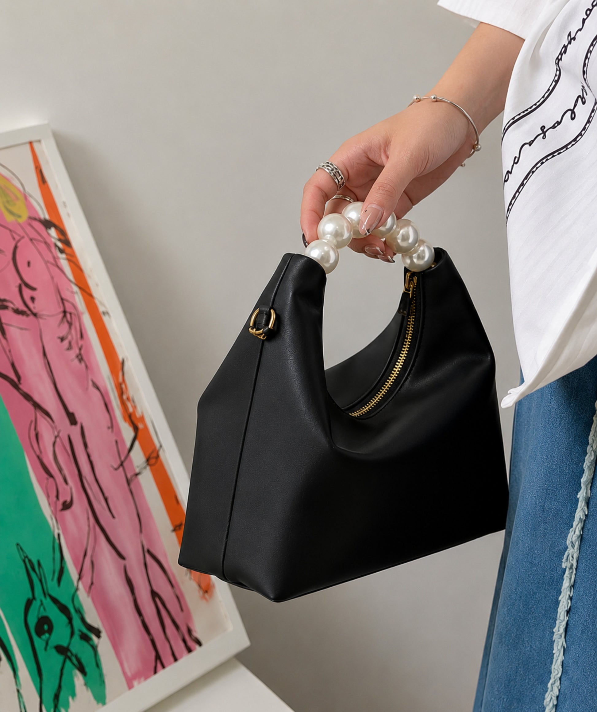 Pearl handle bag in black faux leather held by hand showing soft hobo silhouette gold zipper