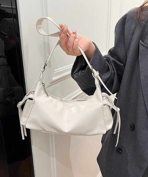 White glossy hobo shoulder bag with adjustable strap, side lace-up pockets, and sleek zip closure design