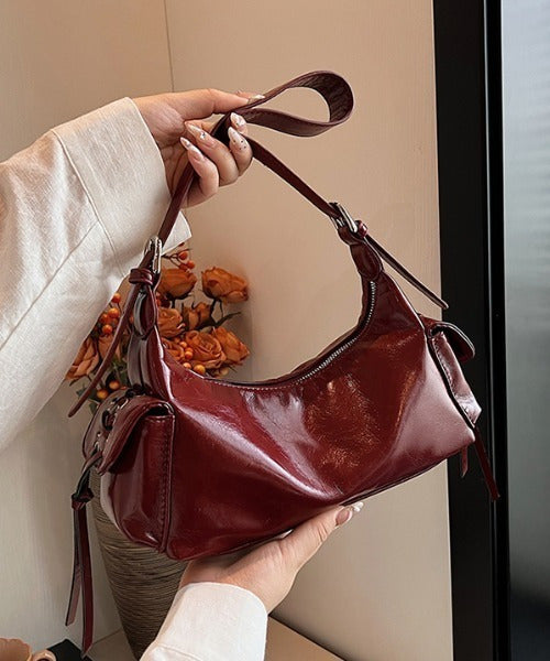Red glossy hobo shoulder bag with adjustable strap, side lace-up pockets, and sleek zip closure design