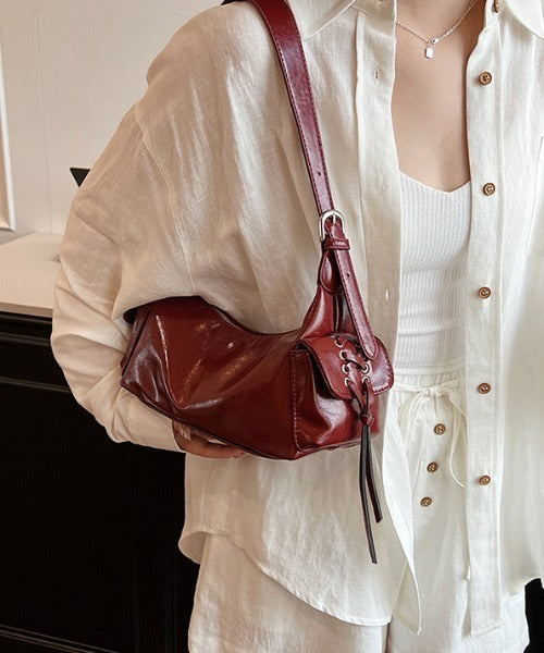 Red glossy hobo shoulder bag with adjustable strap, side lace-up pockets, and sleek zip closure design