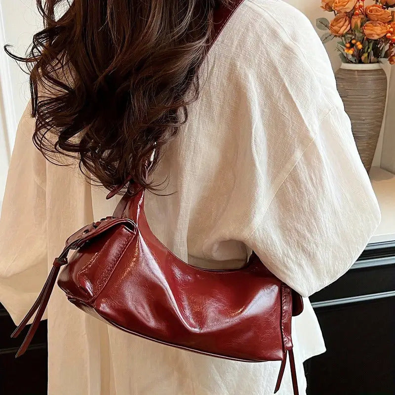 Red glossy hobo shoulder bag with adjustable strap, side lace-up pockets, and sleek zip closure design