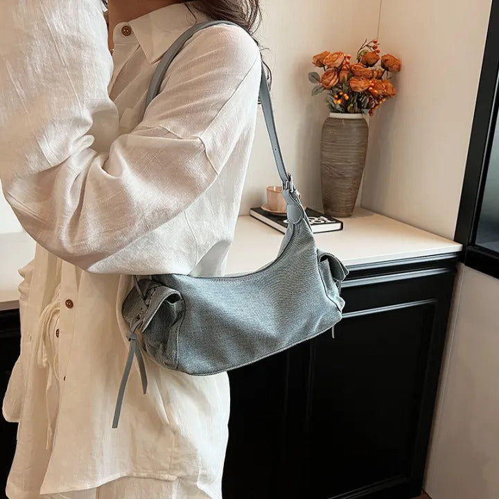 Blue glossy hobo shoulder bag with adjustable strap, side lace-up pockets, and sleek zip closure design