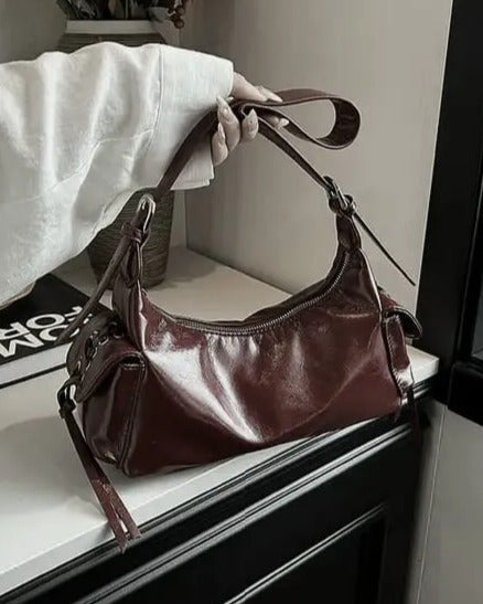 Brown glossy hobo shoulder bag with adjustable strap, side lace-up pockets, and sleek zip closure design