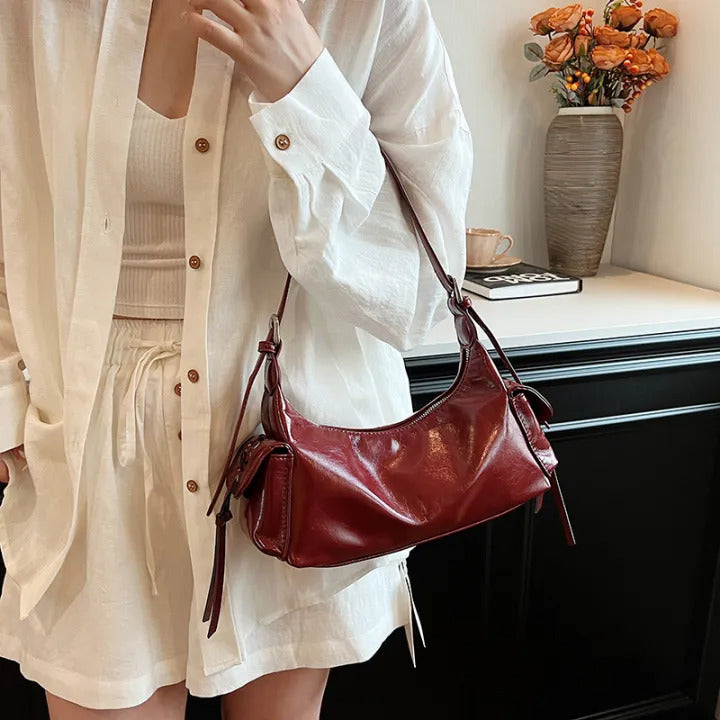 Red glossy hobo shoulder bag with adjustable strap, side lace-up pockets, and sleek zip closure design