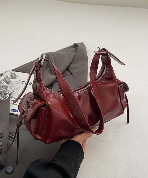 Red glossy hobo shoulder bag with adjustable strap, side lace-up pockets, and sleek zip closure design