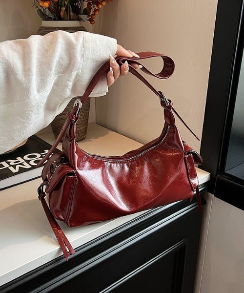 Red glossy hobo shoulder bag with adjustable strap, side lace-up pockets, and sleek zip closure design