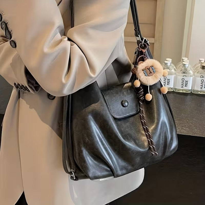 Black slouchy hobo shoulder bag in soft vegan leather with pom-pom keychain, versatile crossbody handbag for women