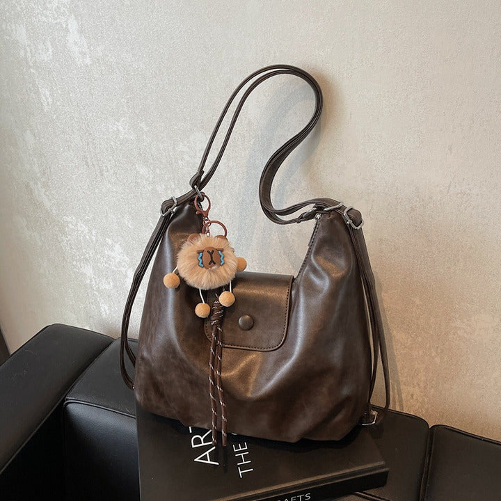 Brown slouchy hobo shoulder bag in soft vegan leather with pom-pom keychain, versatile crossbody handbag for women